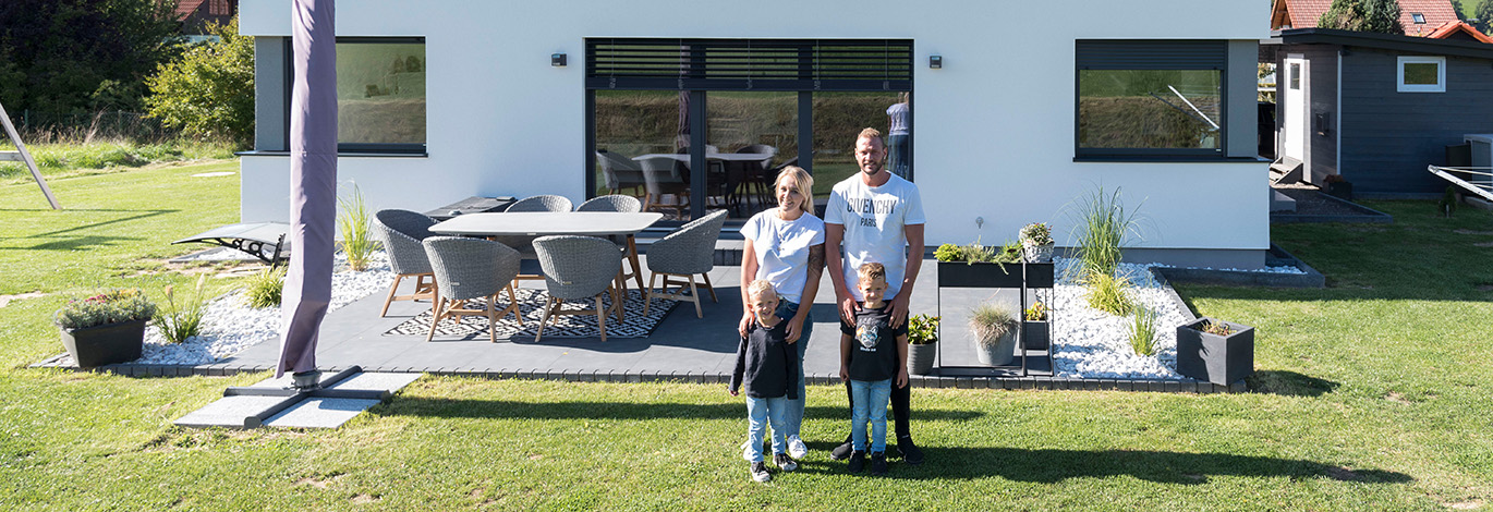 Familie mit zwei Kindern im Garten vor ihrem Fertighaus