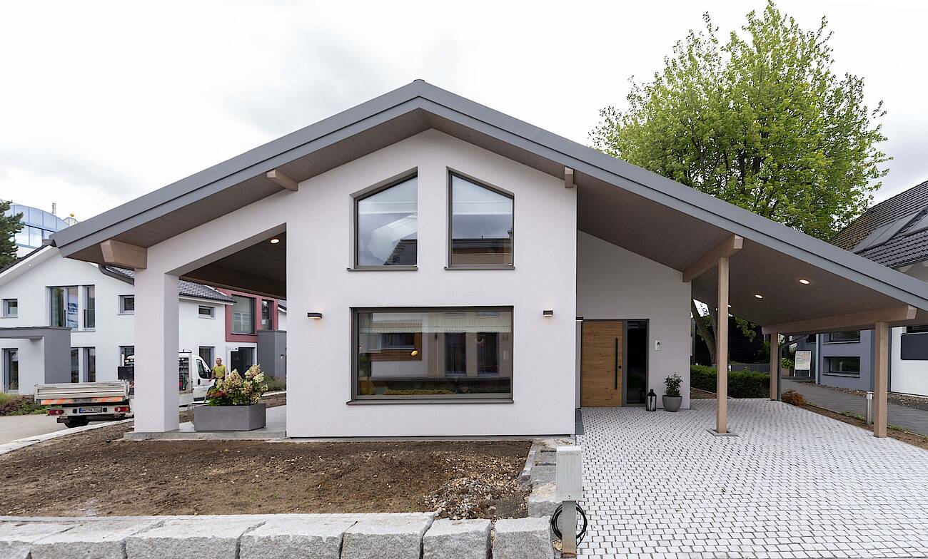 Vorderseite Musterhaus Fellbach. Bungalow mit großen Glasflächen, das Satteldach überspannt Terrasse und Carport