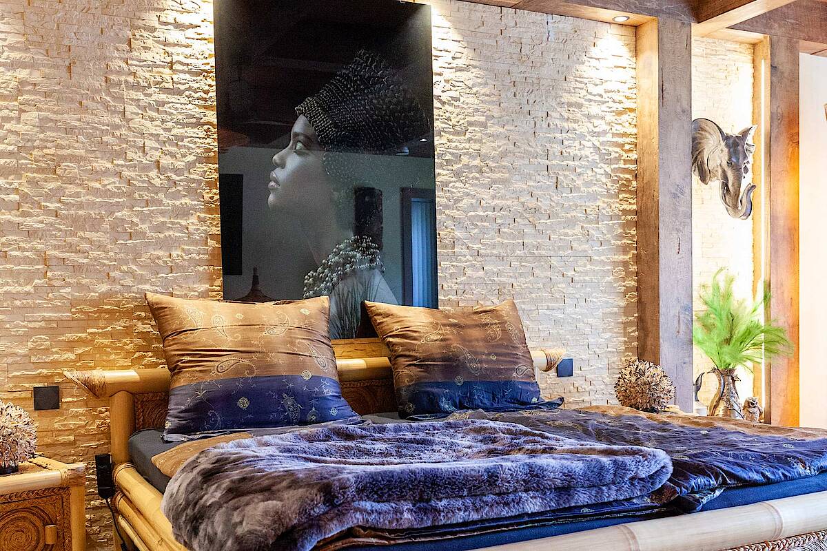 Bett mit Gestell aus Bambusrohren, Lila Bettwäsche und Safari-Dekoration im Hintergrund