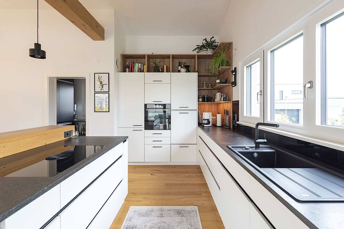 HARTL HAUS Küche mit weißen Möbeln und schwarzen Arbeitsflächen
