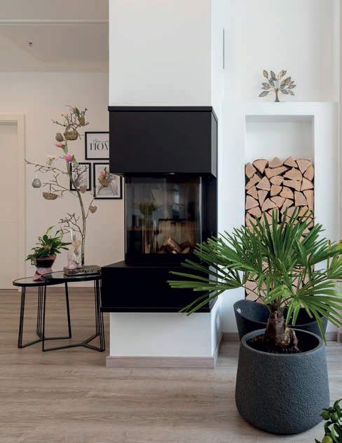 Wohnzimmer mit Kamin, Brennholz und dekorativen Pflanzen im Trend 129 W