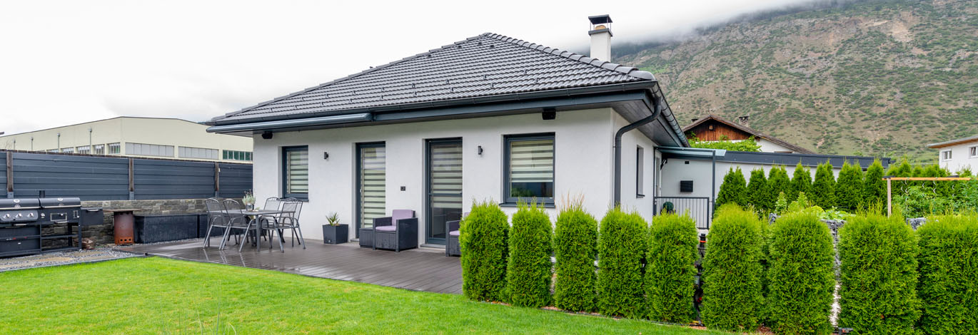 Rückseite des Bungalows mit Terrasse und Garten und Hecke rechts