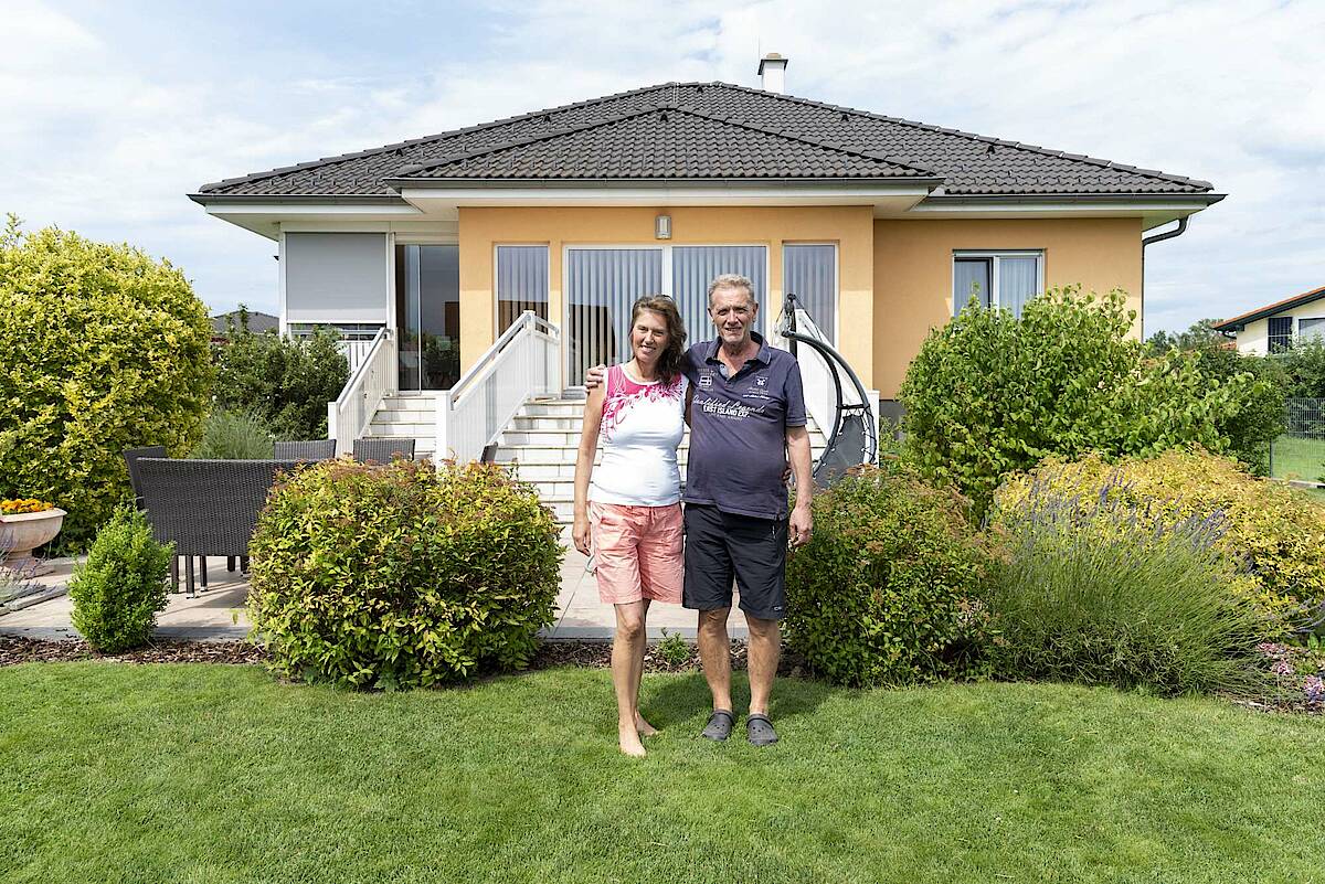 Mann und Frau vor ihrem Haus im Garten, Blick in die Kamera