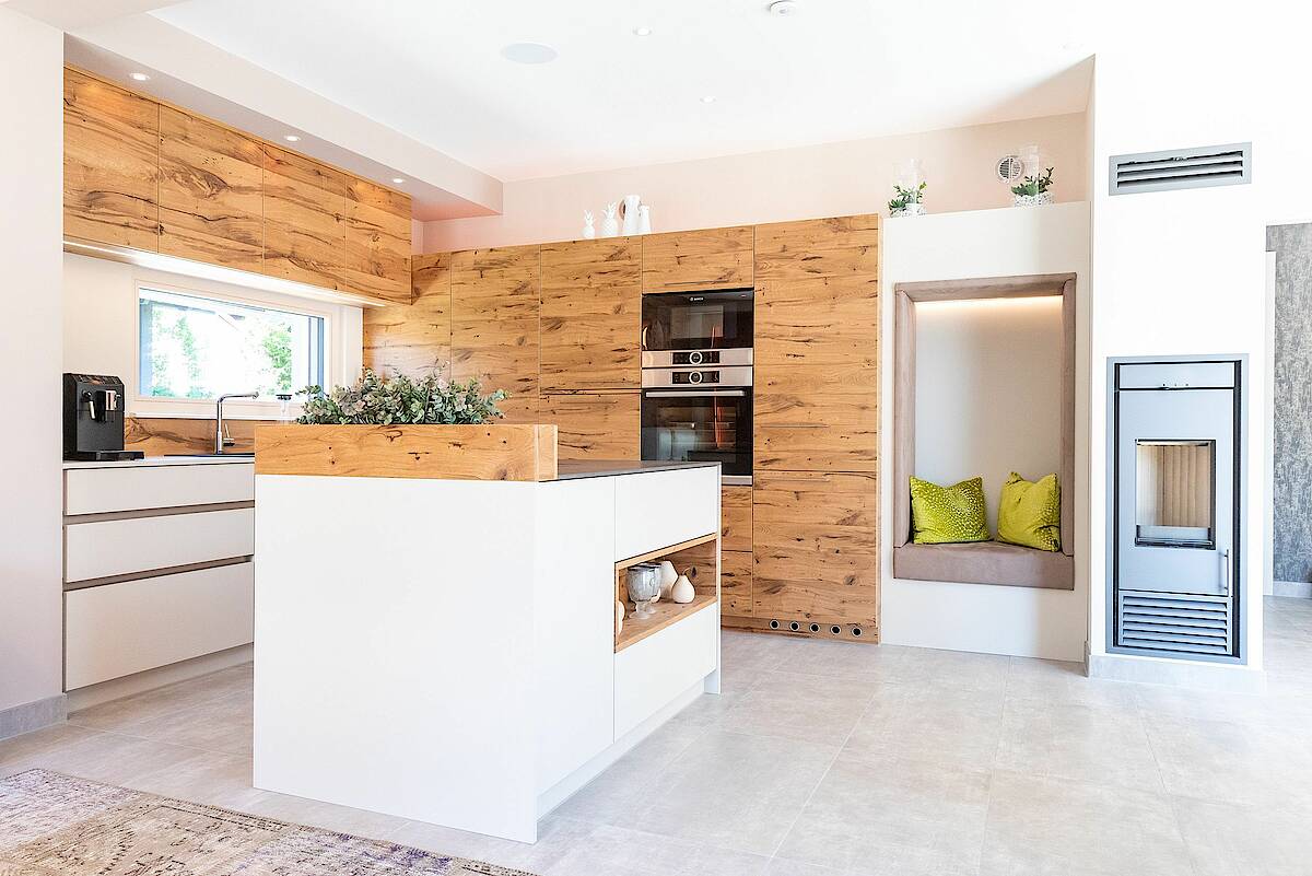 Hartl Haus Einbauküche mit Kücheninsel. Weiße Möbel mit Naturholzflächen