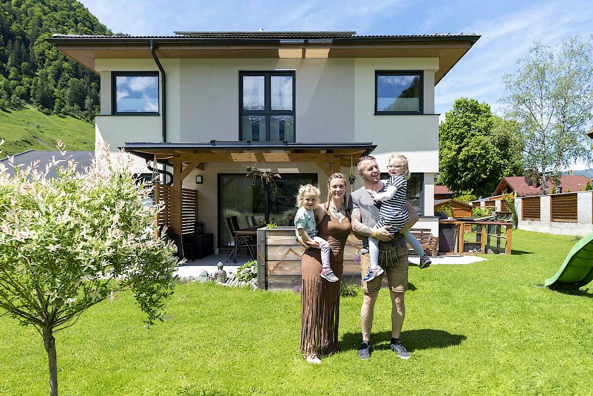 Familie mit zwei Kindern im Garten ihres Einfamilienhauses mit Bergblick