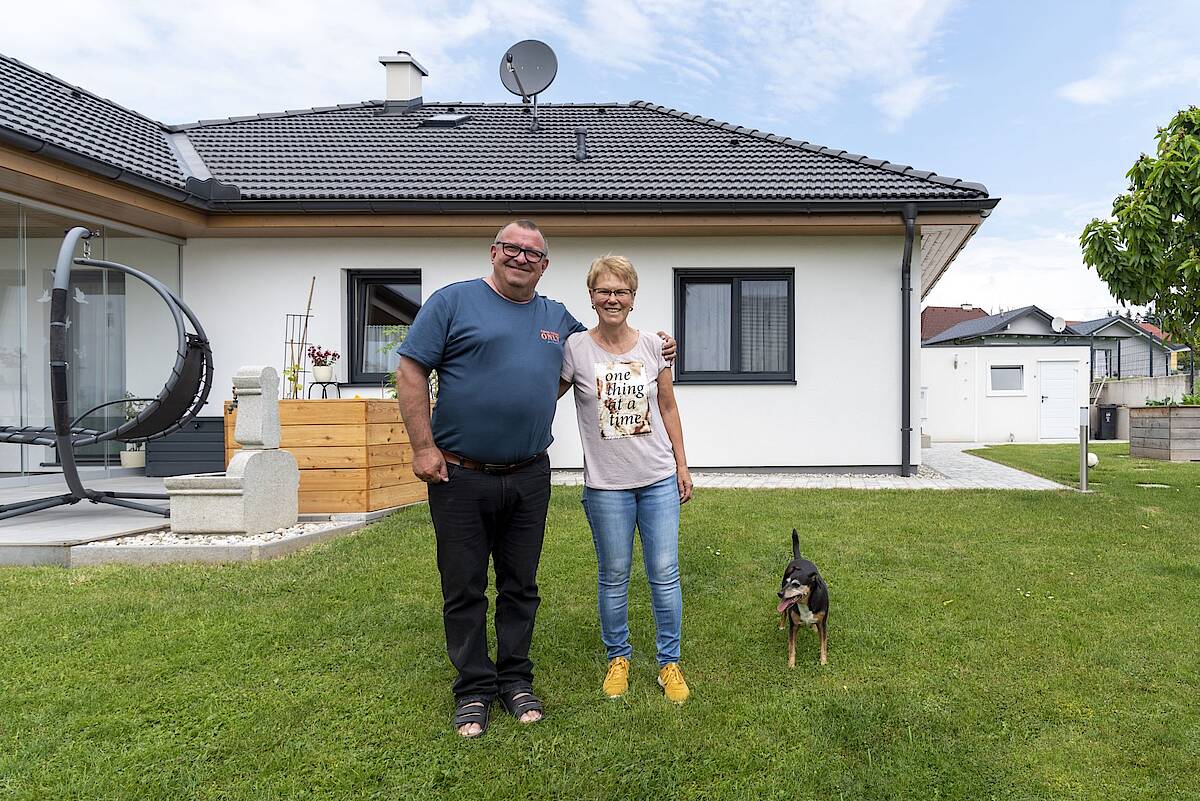 Älteres Paar mit Hund im Garten vor ihrem Fertighaus-Bungalow