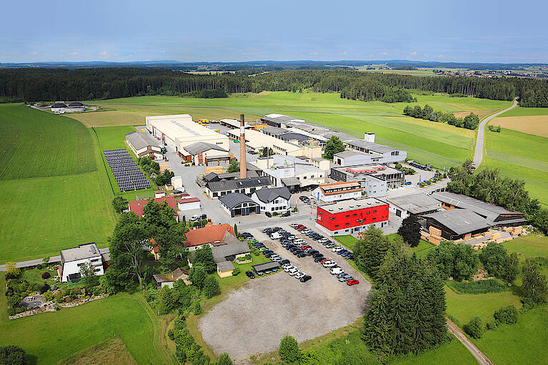 Luftaufnahme des Hartl Haus Werks. Werkshallen und Gebäude inmitten grüner Landschaft